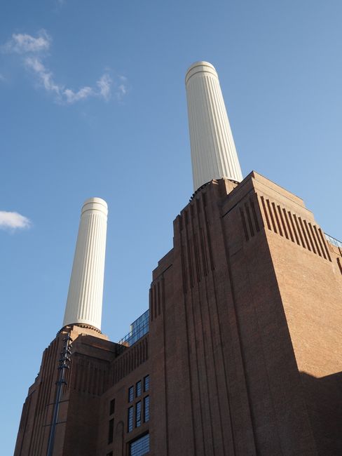 A close-up view of the Battersea Power Station in Wandsworth, featuring two large, white, cylindrical chimney stacks with ribbed textures, positioned atop a historic brick building with a reddish-brow